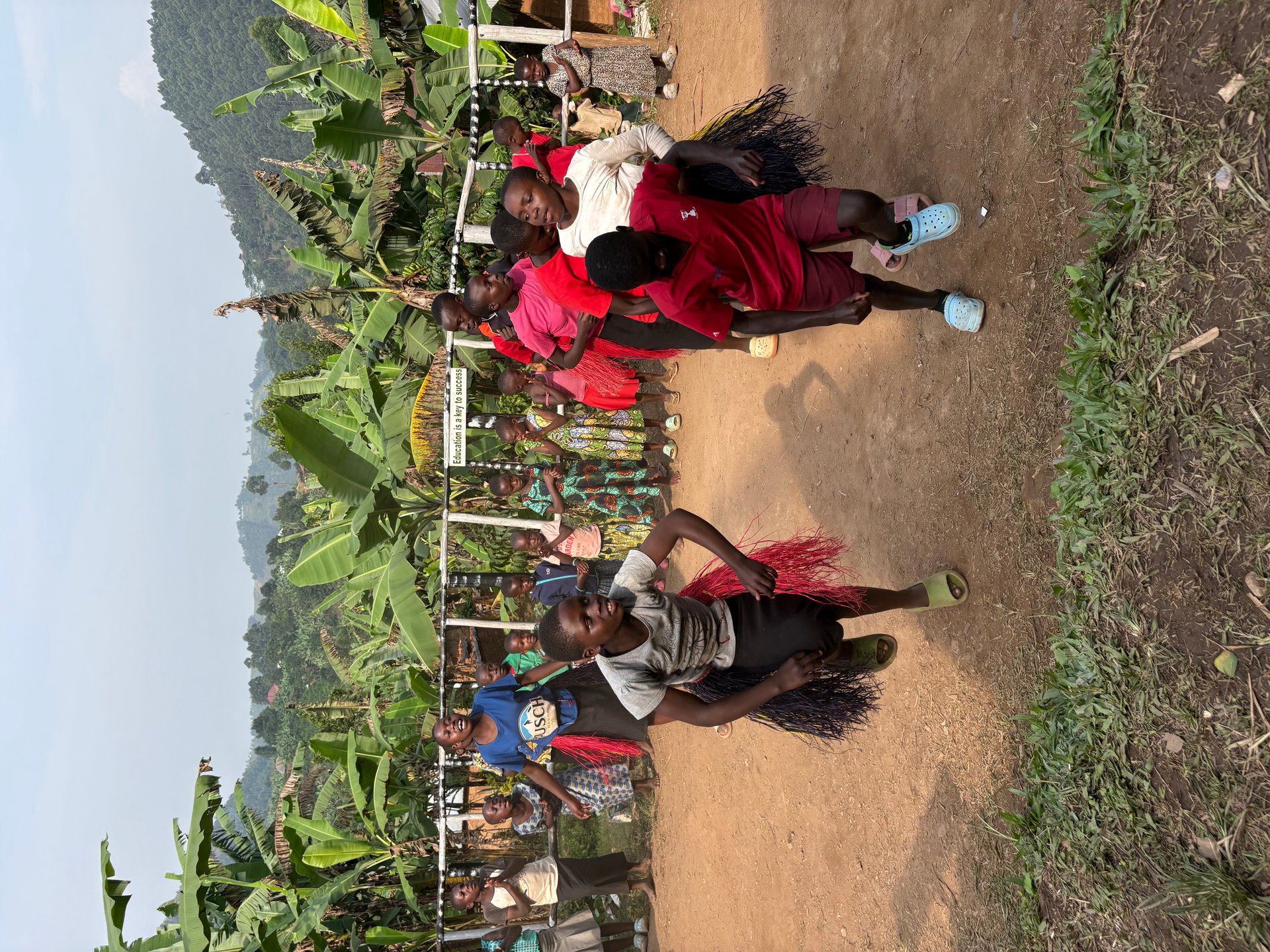 Children performing a traditional Ugandan dance with raffia costumes at the Buhoma orphanage, banana trees and green hills behind