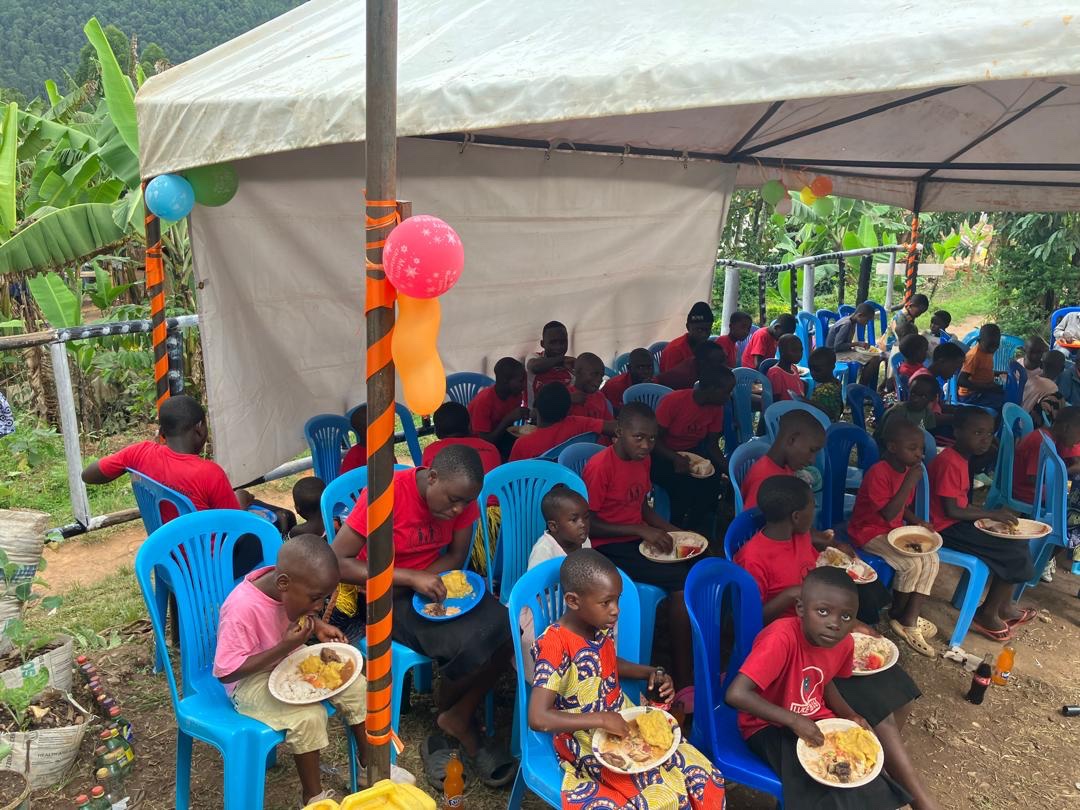 Children eating together under a tent at a community gathering in Buhoma