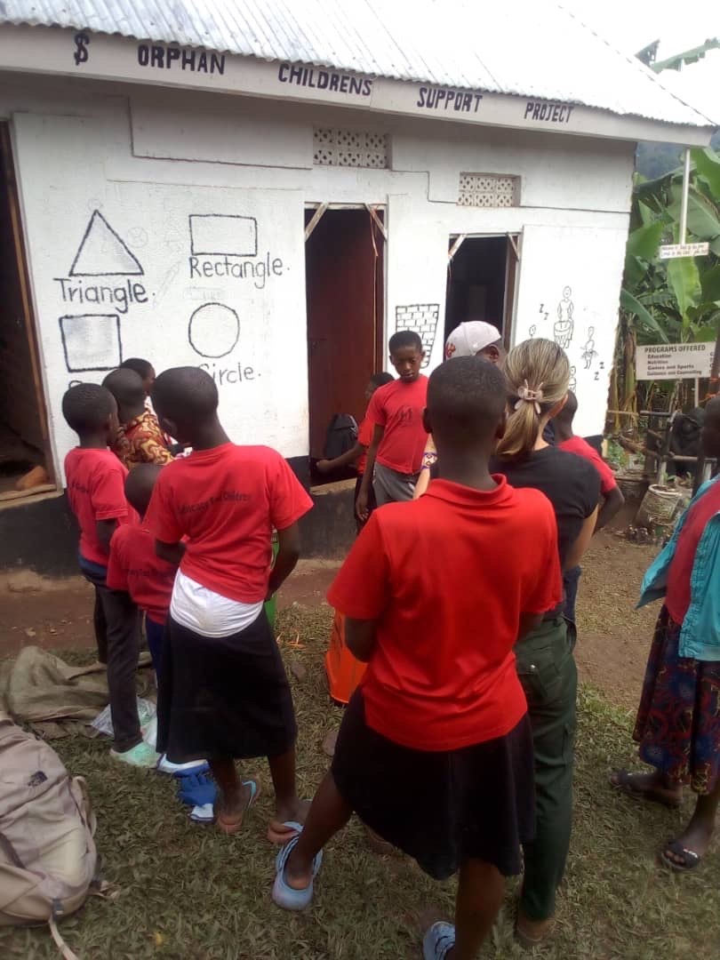 Children in red shirts gathering at the Orphan Children's Support Project building with geometric shapes on walls