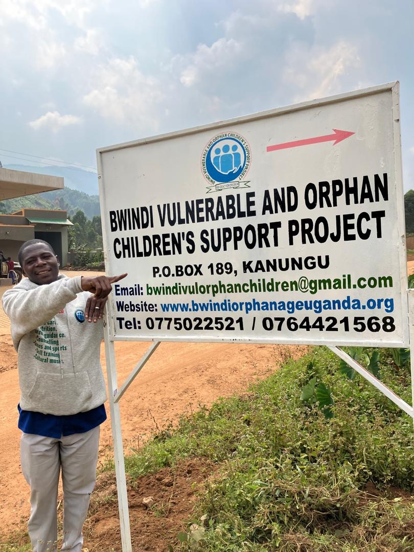 Man pointing at the sign of the Bwindi Vulnerable and Orphan Children's Support Project in Kanungu
