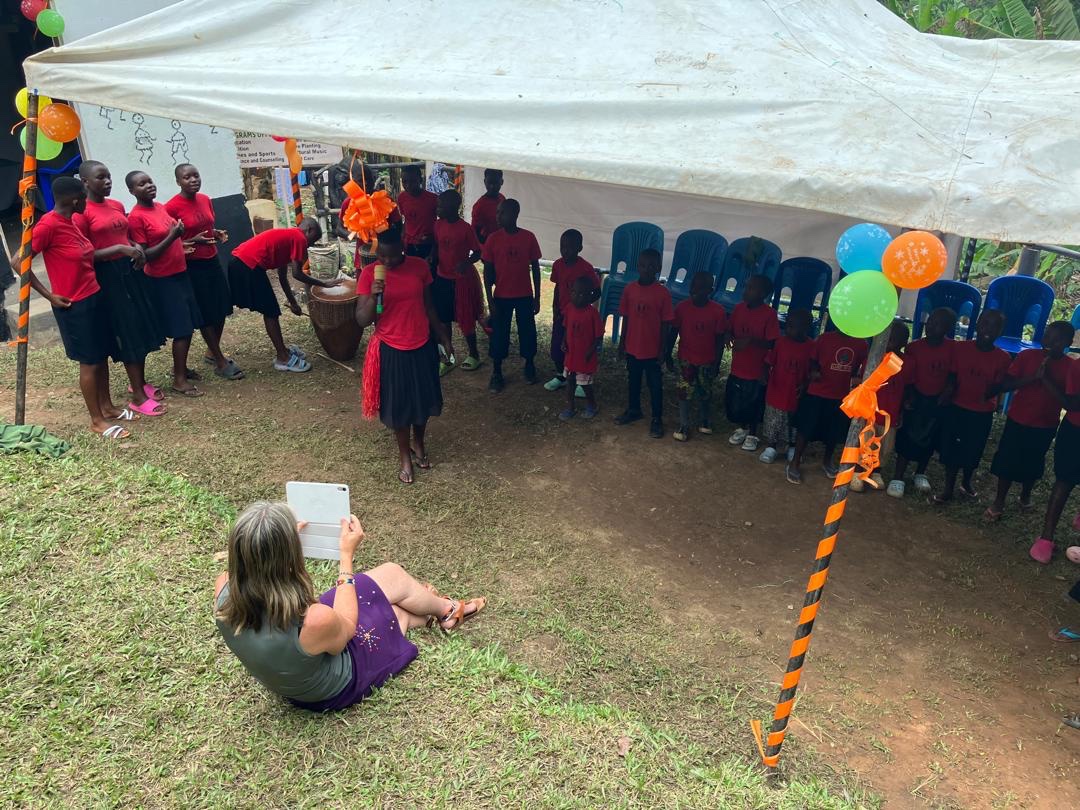 Children in red shirts performing under a decorated tent at a community event in Buhoma