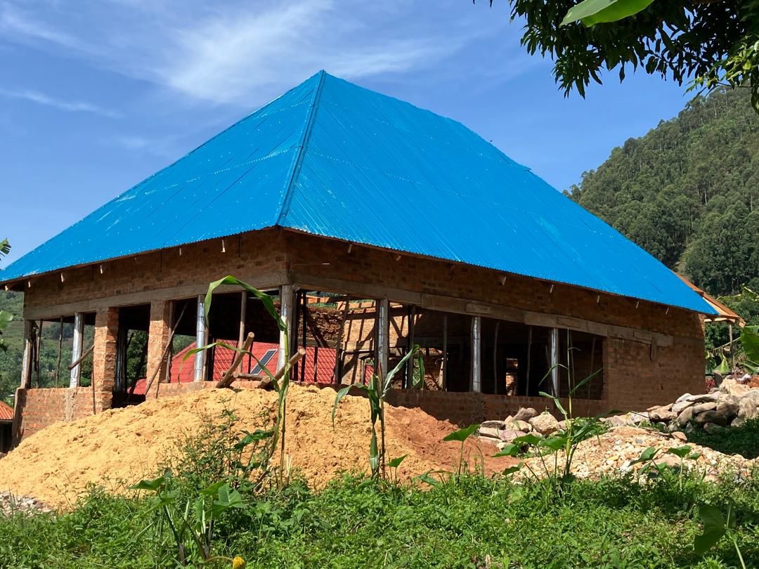 HopeKitchen building under construction with blue corrugated roof in Buhoma, rainforest hills in the background