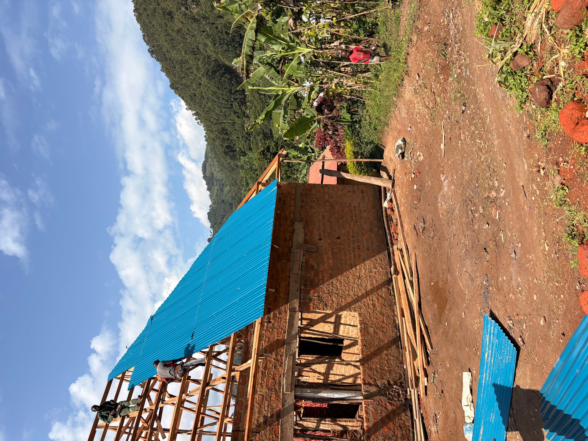 HopeKitchen under construction in Buhoma — blue corrugated roofing, wooden trusses and red-earth walls against green hills