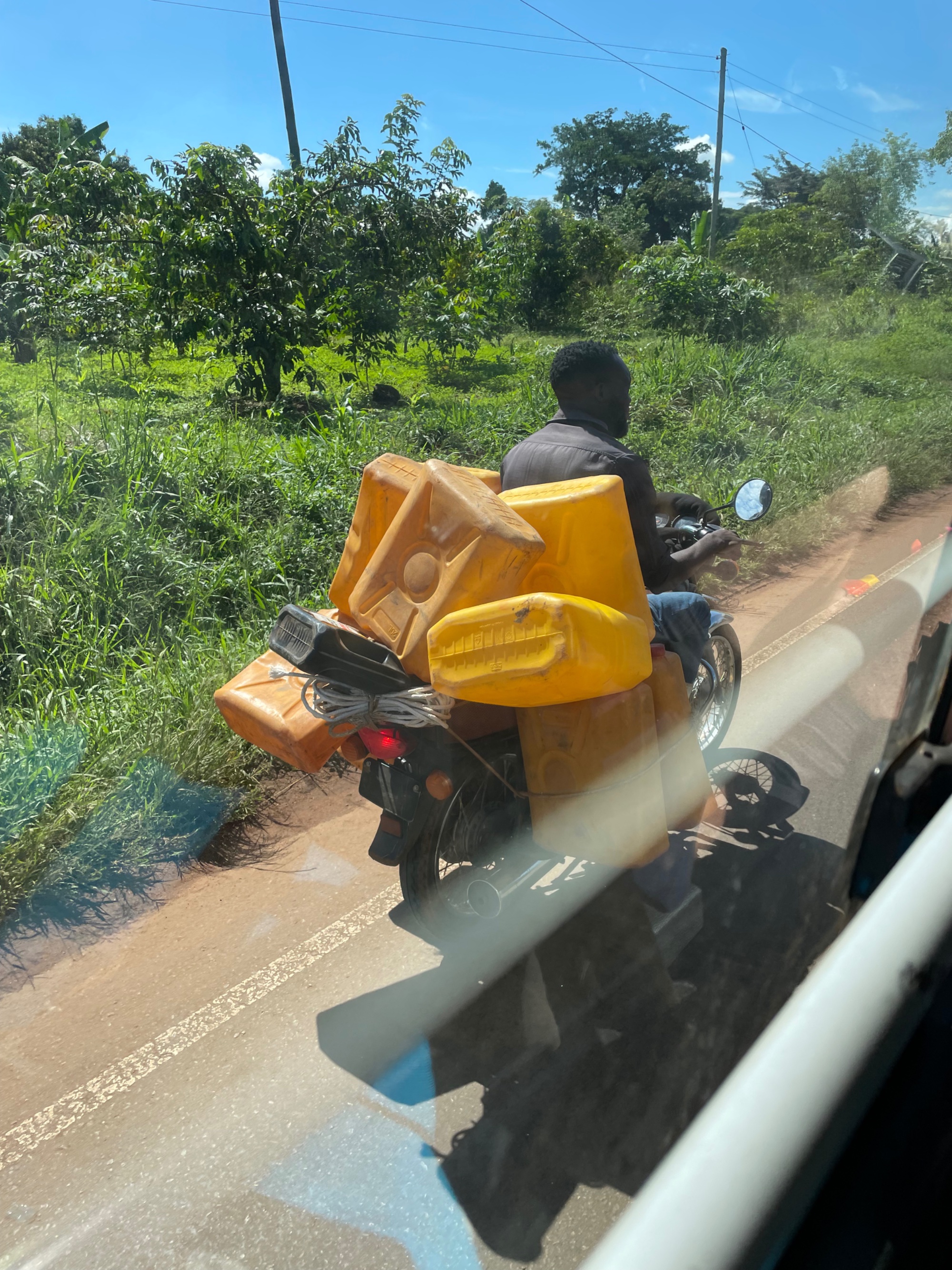 BodaBoda motorcycle loaded with yellow jerrycans of water on a red-earth road in rural Uganda